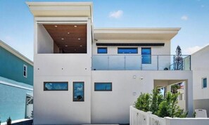 Um edifício moderno de dois andares com telhado plano, janelas grandes e uma varanda no andar superior.