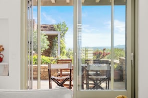 Ein Zimmer mit einer Schiebeglastür, die auf eine Terrasse mit Steinwand, Holzmöbeln und Landschaftsblick führt.