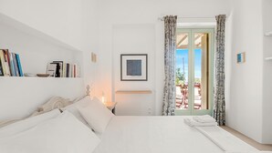 Ein Schlafzimmer mit Bett, Nachttisch, Lampe, Bücherregal, gerahmtem Bild und Blick durch eine Tür.