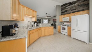 A modern kitchen with granite countertops, wooden cabinets, a white refrigerator, and a ceiling fan. - Lakefront retreat w/Private pool- Winter/Mid-Term visitor discount available (Fort Mohave)