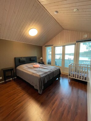 A bedroom with a bed, a nightstand, a crib, a window, and a door leading to a balcony.