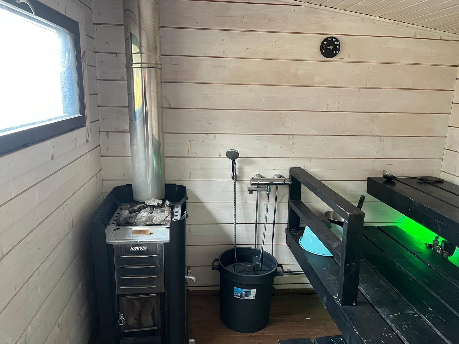A sauna room with a Harvia sauna, a black bucket, and a green-lit bench.