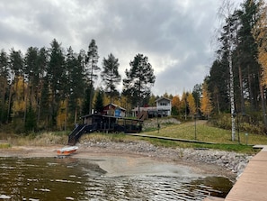 A lakeside cabin with a dock, surrounded by dense forest and autumn foliage.