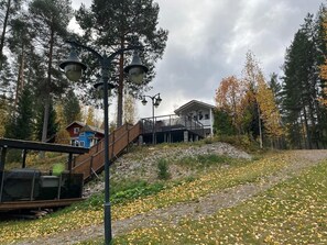 A wooden bridge, a building with a balcony, and a forested area.