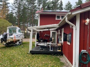 A red cabin with a covered porch, a boat on a trailer, and a gym setup.