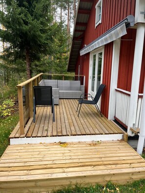 A wooden deck with a seating area, a red building with white trim, and a forested background.
