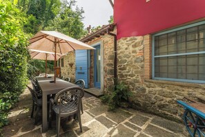 A stone building with a blue door, a table with chairs, and an umbrella. - Charming mill nestled in the woods, convenient for visiting all of Tuscany (Colle di Buggiano)