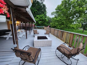 A covered deck with outdoor furniture, a fire pit, and a view of the surrounding greenery.