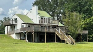 A large house with a green roof, multiple decks, and a staircase leading to the main entrance. - River House with dock & boat slip, perfect for Alabama & Mississippi game days (Columbus)