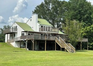 A large house with a green roof, multiple decks, and a staircase leading to the main entrance.