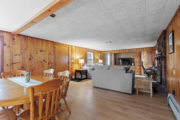 A wooden-paneled room with a dining table, chairs, a sofa, and a television. - Steps to Colonial Acres Beach Spacious Home (Yarmouth)