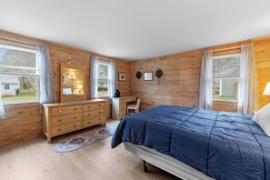 Ein Schlafzimmer mit Holzwänden, einem Bett, einer Kommode, einem Schreibtisch und einem Stuhl.