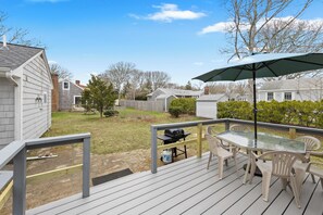 Een terras met een tafel en stoelen met glazen blad, een barbecue en een parasol.