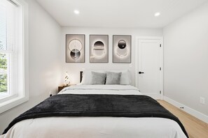 Un dormitorio con cama, mesita de noche, ventana y tres obras de arte colgadas en la pared.