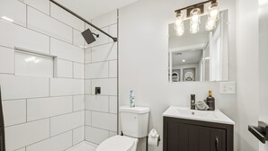 Ein modernes Badezimmer mit Toilette, einer Dusche mit Regendusche, einem Waschbecken mit Spiegel und einem dunklen Schrank.