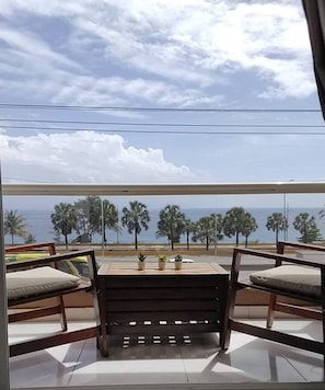 A balcony with a view of the sea, palm trees, and a wooden table with chairs. - Relaxing Ocean Views (Santo Domingo Este)
