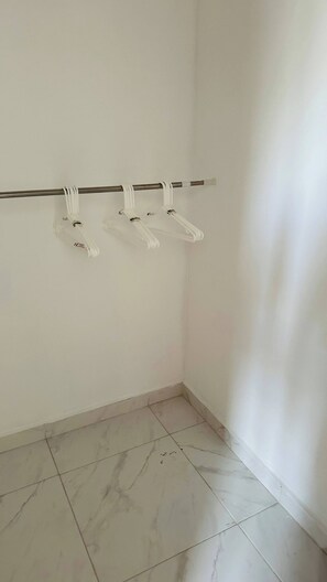 A corner of a room with a white wall, a marble-tiled floor, and a metal rod with white hangers. - Relaxing Ocean Views (Santo Domingo Este)