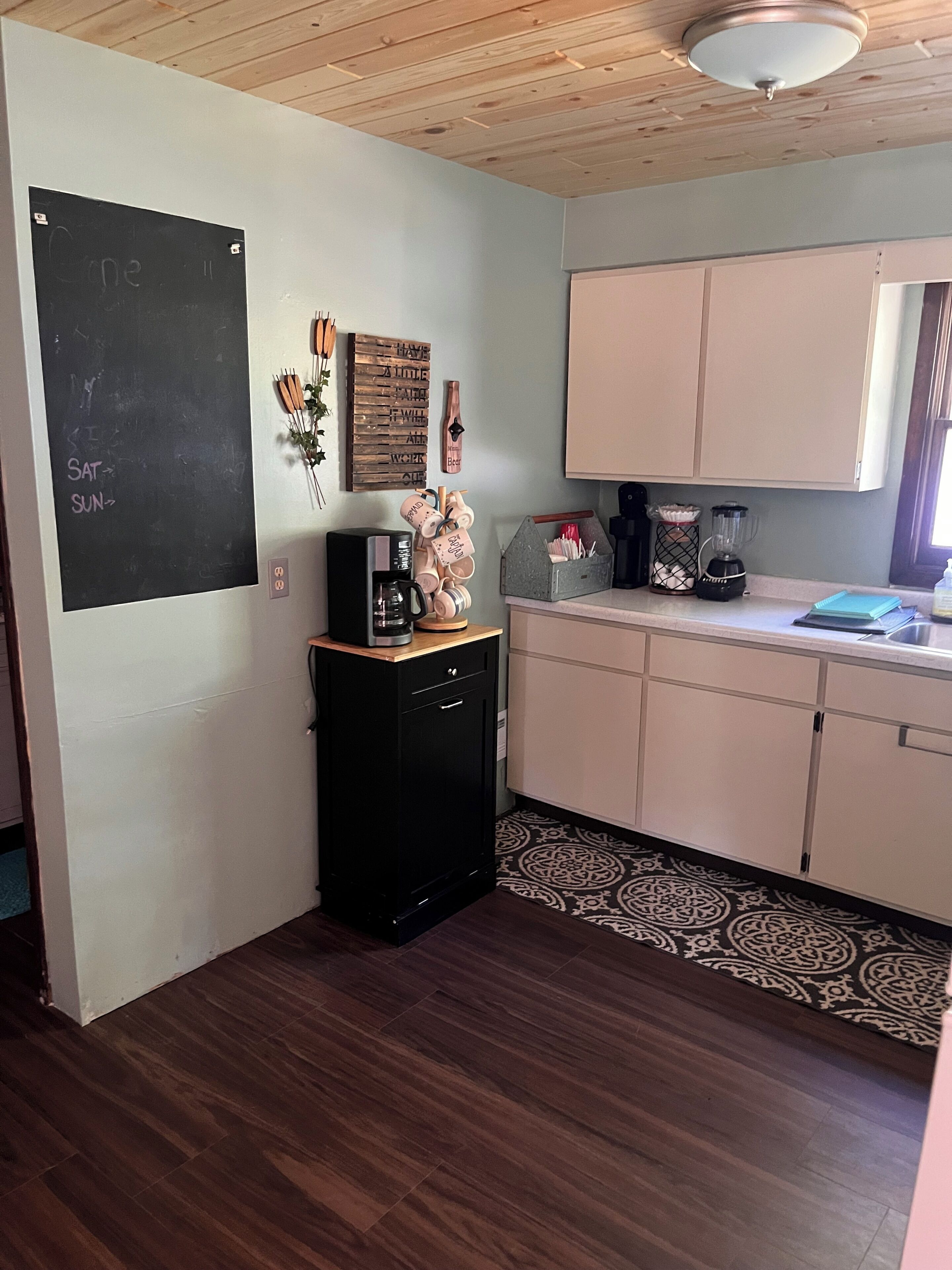 A kitchen with a blackboard, wooden cabinets, a coffee maker, and a decorative mug holder.