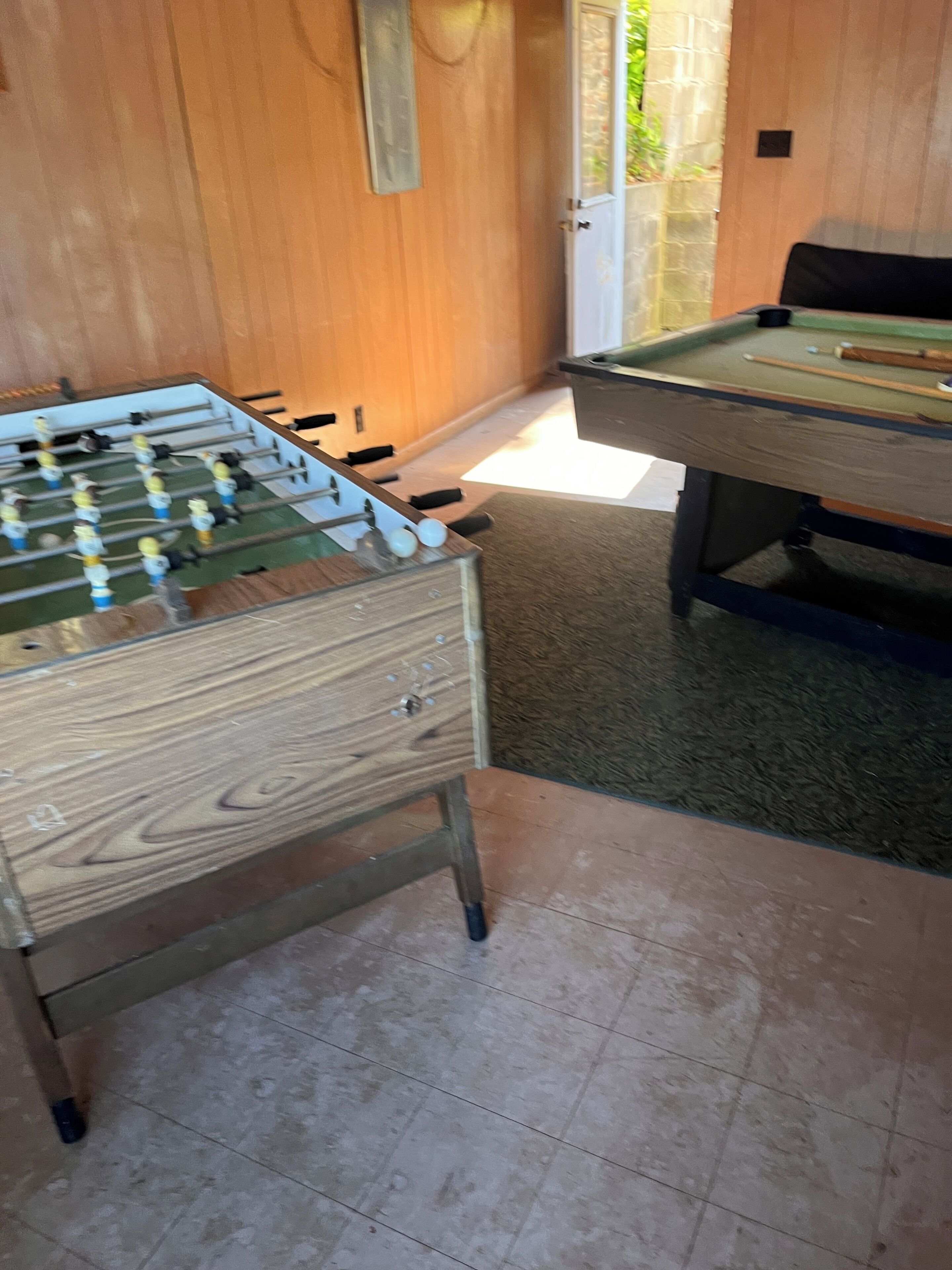 Un tavolo da calcio e un tavolo da biliardo in una stanza con pareti in legno e pavimento piastrellato.