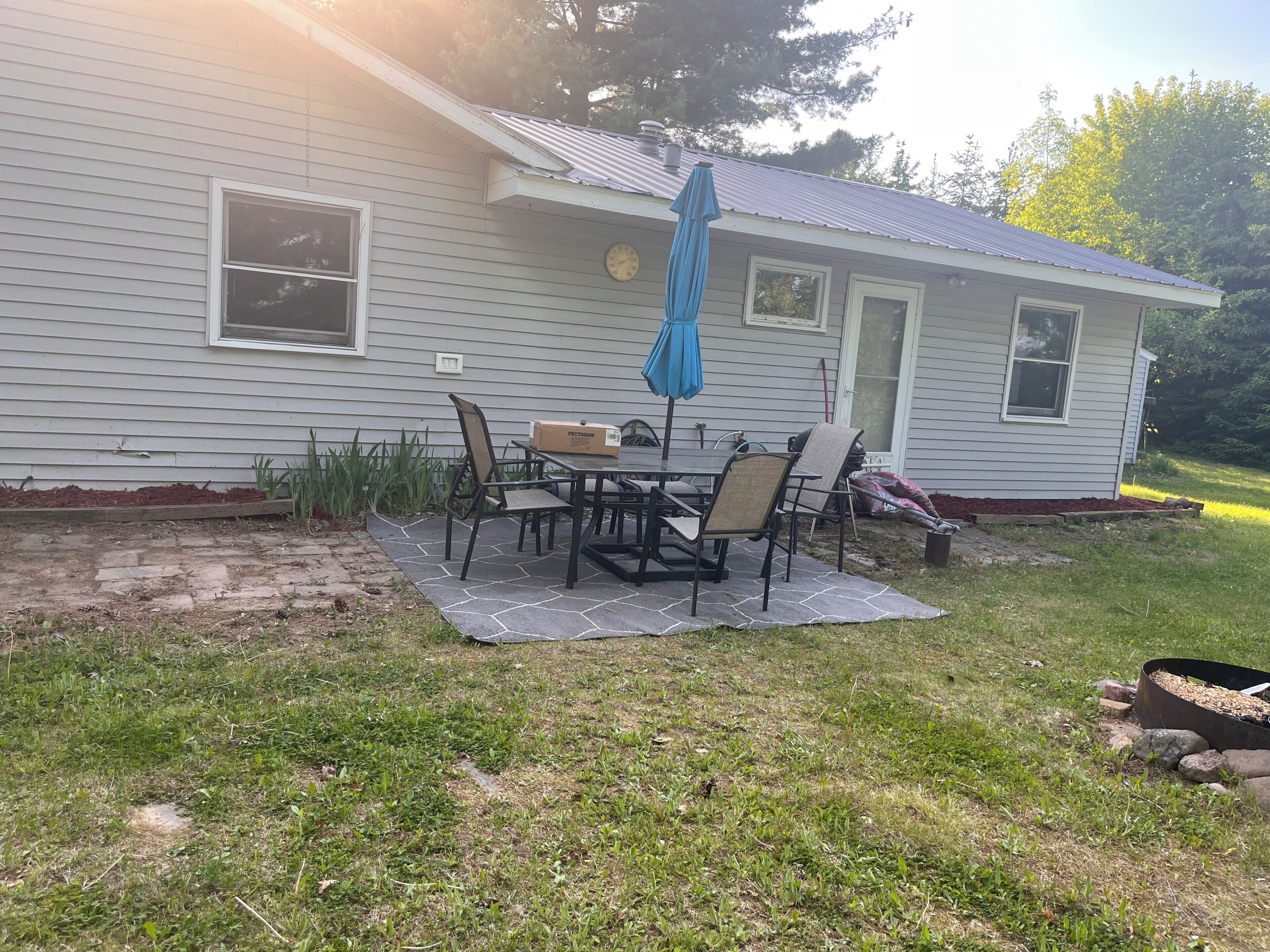 A house with a patio area featuring a table and chairs, a clock, and a mailbox.