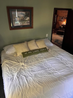 Una cama con una colcha de estampado geométrico, un cuadro enmarcado encima y un cartel sobre la cama que dice 'WE ARE LAKE PEOPLE'.