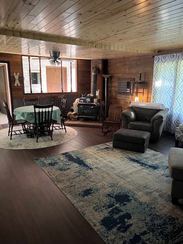 Una sala de estar acogedora con techo de madera, chimenea, una mesa de comedor con sillas y un sofá.