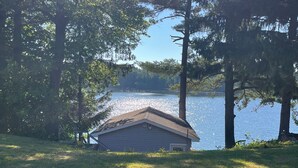 A small cabin with a sloped roof, surrounded by grass and trees, overlooking a calm lake. - Rustic recently updated 3-bedroom cabin with AC on Upper Turtle Lake. (Turtle Lake)