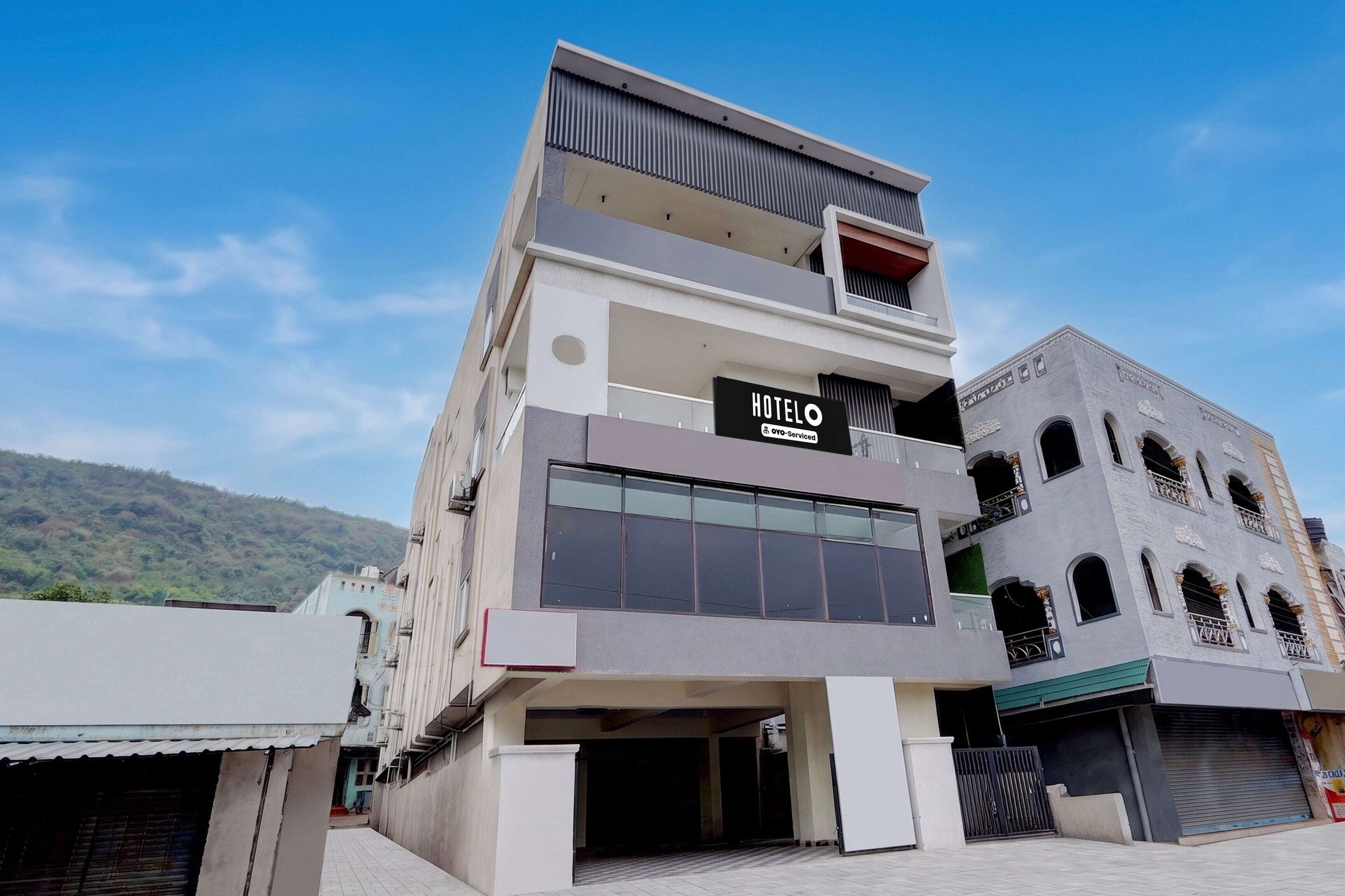 Un hotel moderno con un letrero llamativo, un acceso cubierto y vistas a un paisaje montañoso.