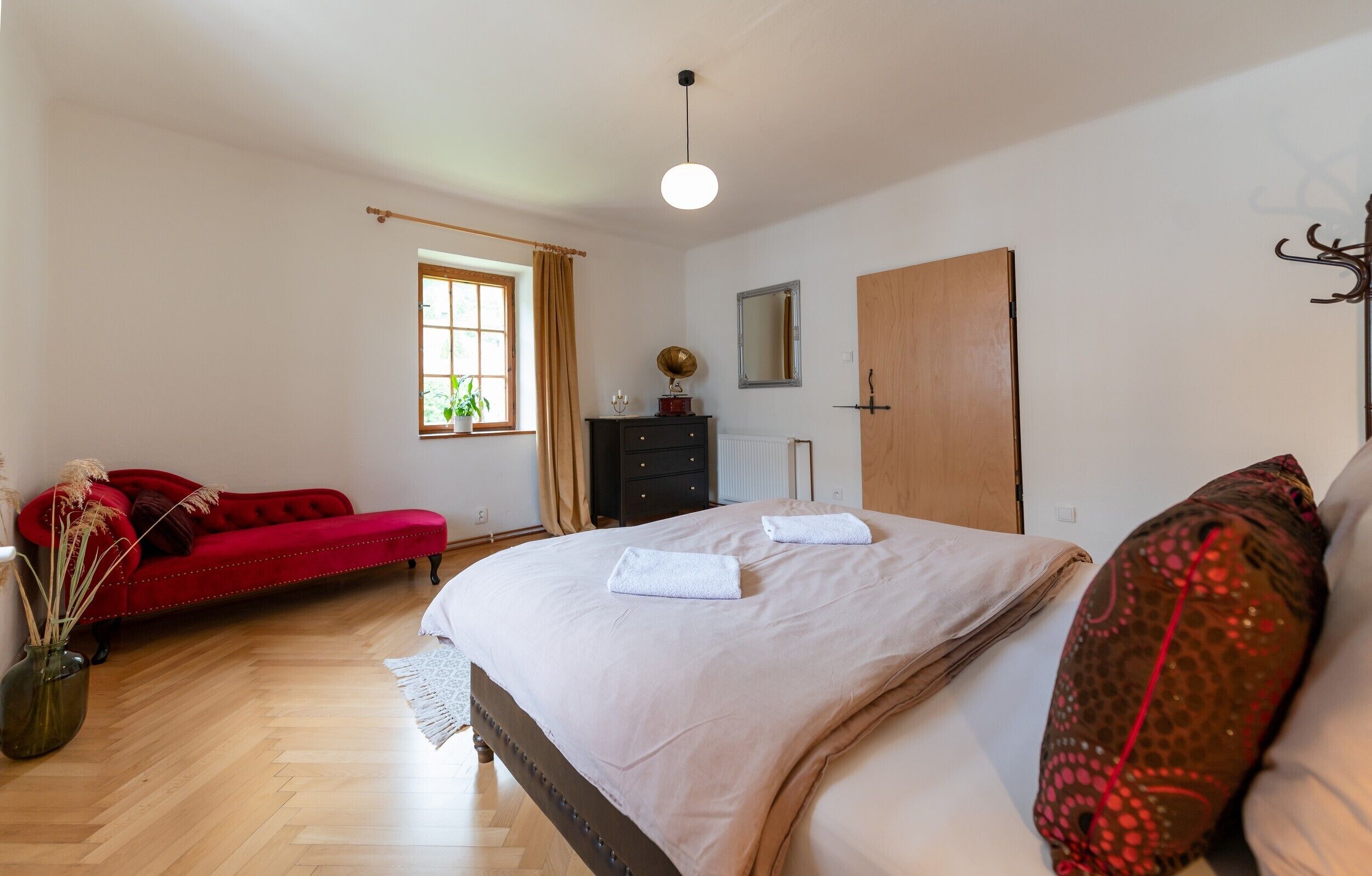 Une chambre à coucher avec un lit, un canapé rouge, une commode, un miroir et une fenêtre.