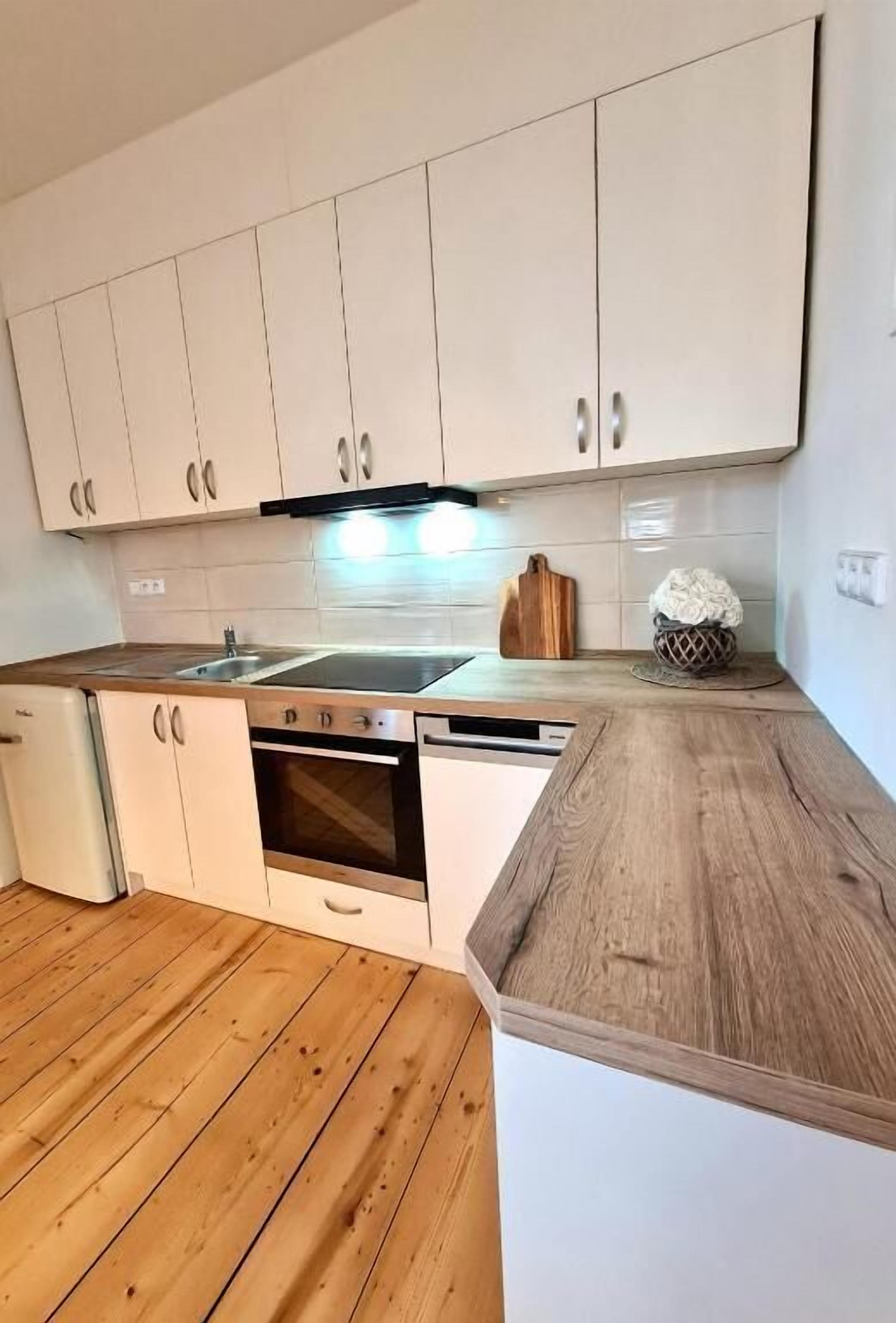 A kitchen with white cabinets, a wooden countertop, a dishwasher, and an oven.