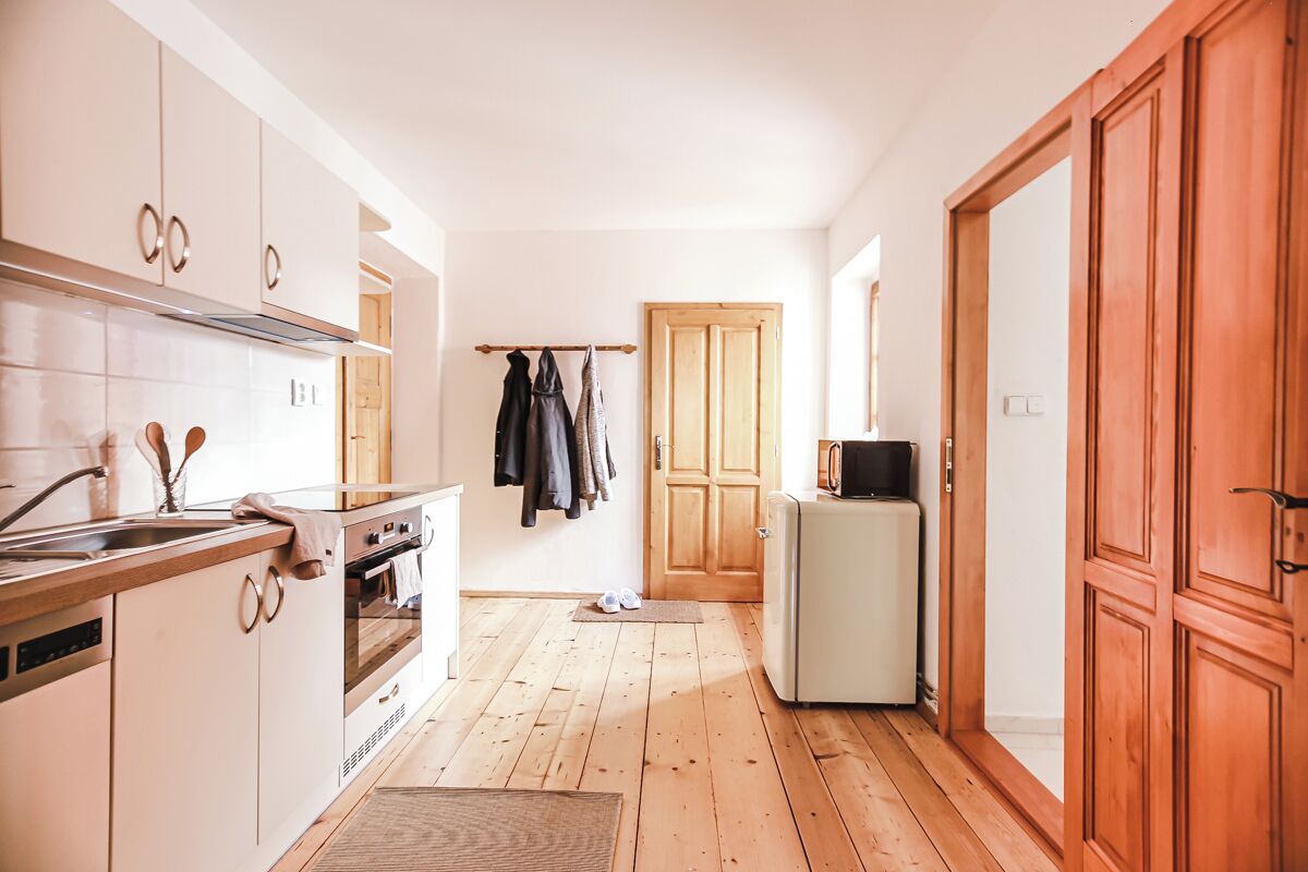 A kitchen with wooden cabinets, a stove, a refrigerator, and a door leading to another room.