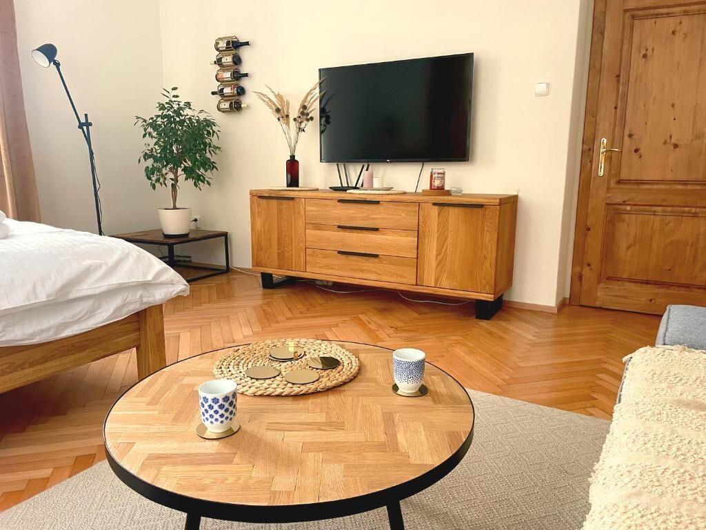 Une pièce comprenant un lit, une table ronde en bois avec deux tasses, un téléviseur fixé au mur, un meuble en bois et une porte.