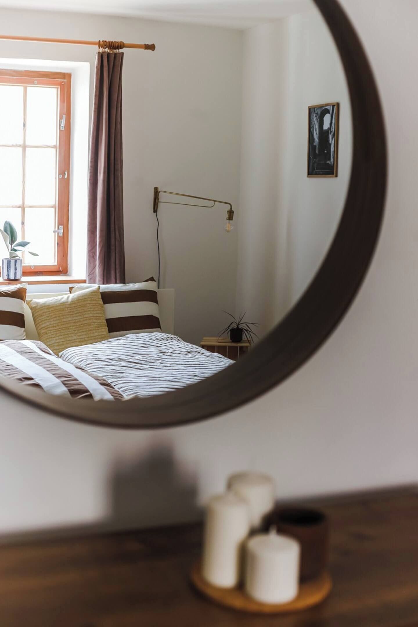Une chambre à coucher avec un lit, une table de chevet avec des bougies, une fenêtre avec des rideaux et une lampe fixée au mur.