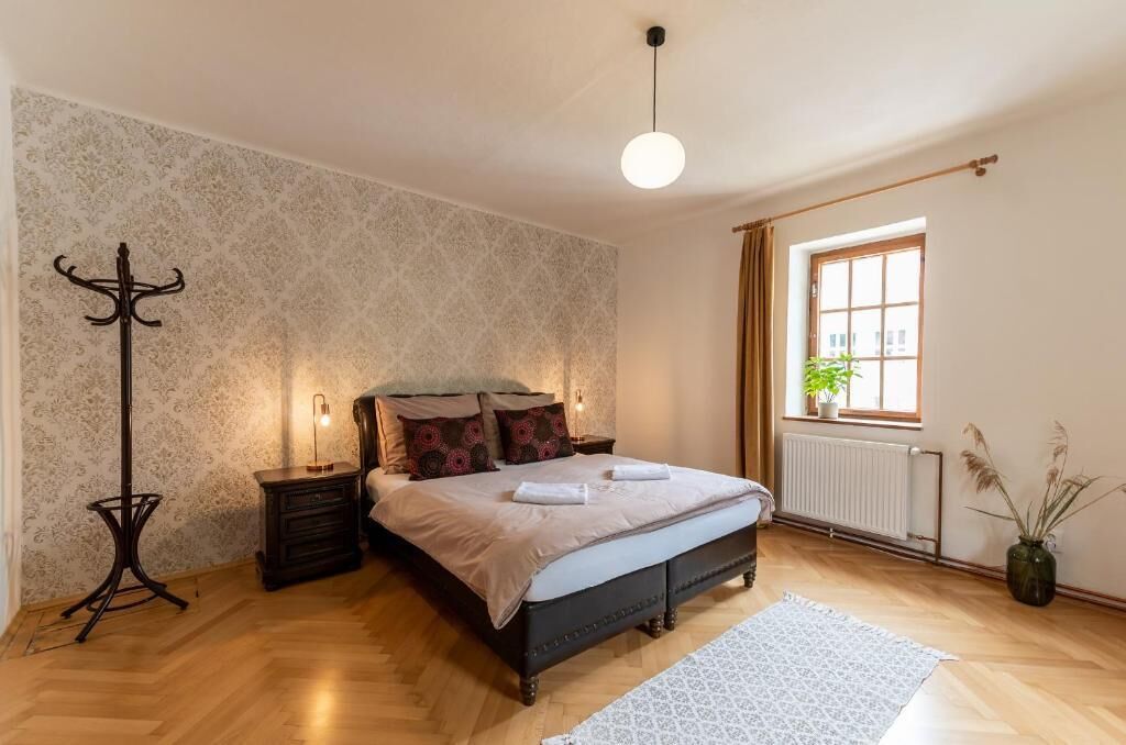 Un dormitorio con cama, mesitas de noche, una lámpara de pie, ventana con cortinas y un radiador.