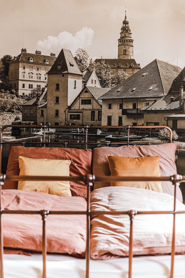 A bed with metal headboard and pillows, a view of buildings and a tower in the background.