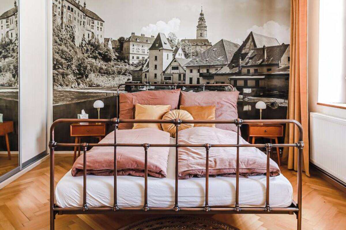 A bedroom with a bed, a round woven rug, a cityscape mural, and a hanging light fixture.