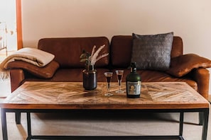 Una mesa de centro de madera con un florero, dos vasos y una botella.