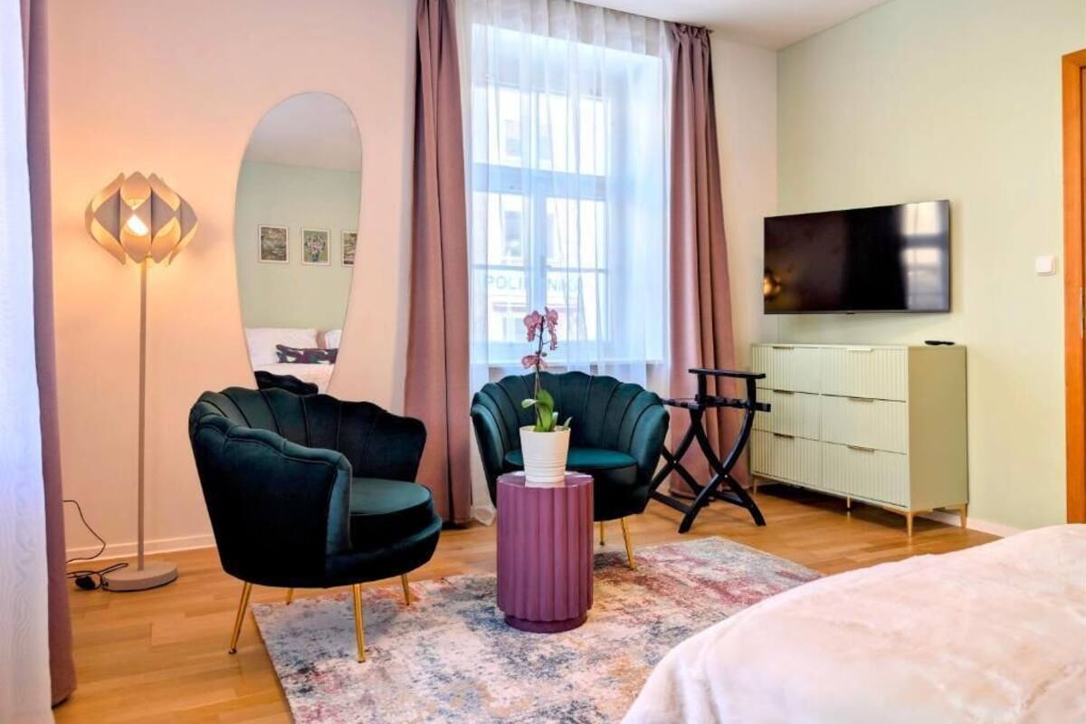 A modern bedroom with a bed, two chairs, a small table, a TV, a wardrobe, and a window with curtains.