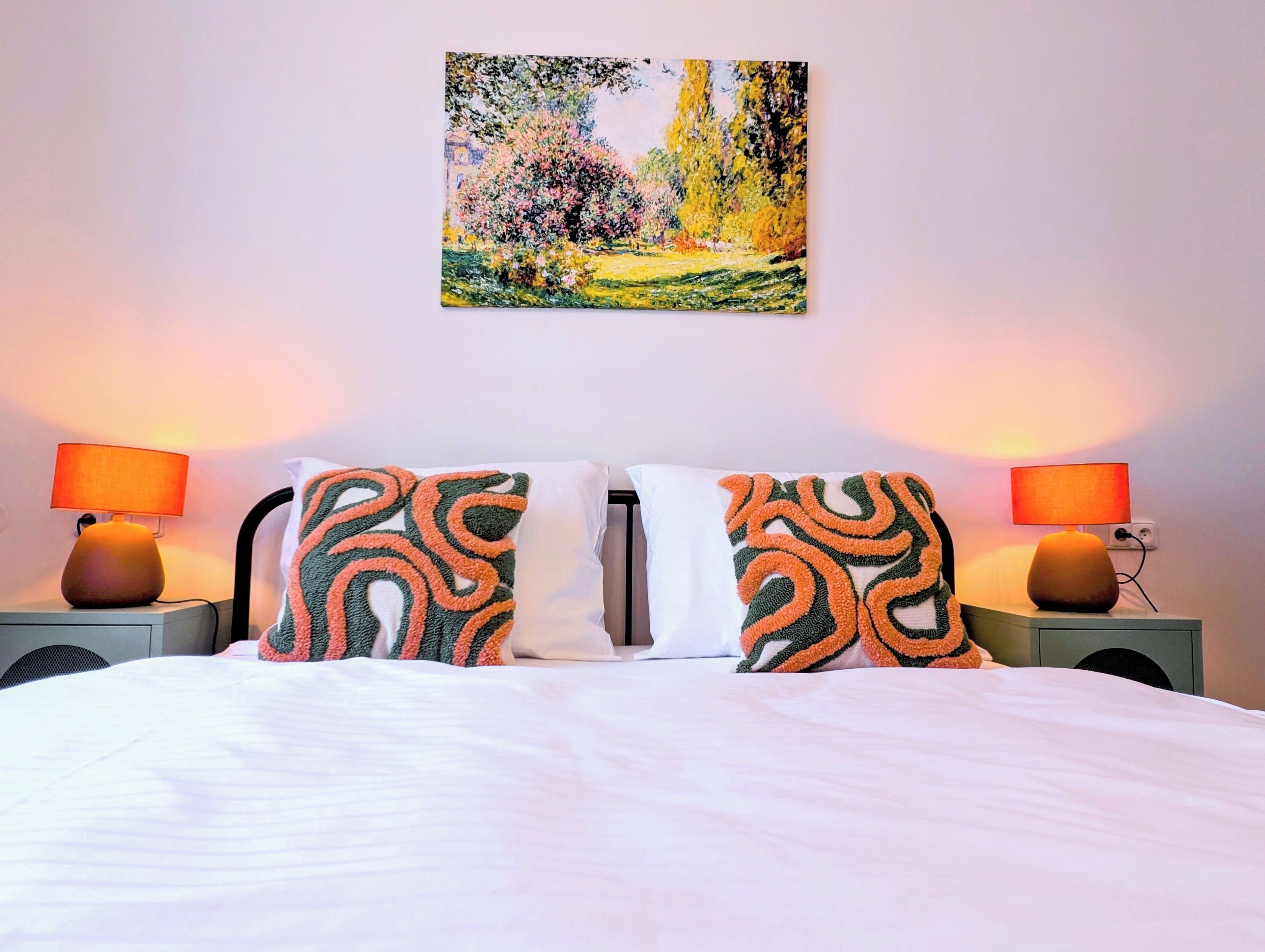 A hotel room with a bed, two bedside lamps, a painting on the wall, and a patterned pillow.