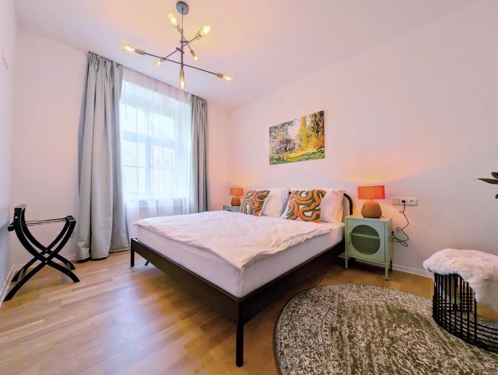 A bedroom with a bed, bedside lamps, a painting, a chair, and a rug.