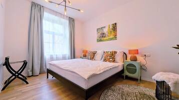 A bedroom with a bed, bedside lamps, a painting, a chair, and a rug.