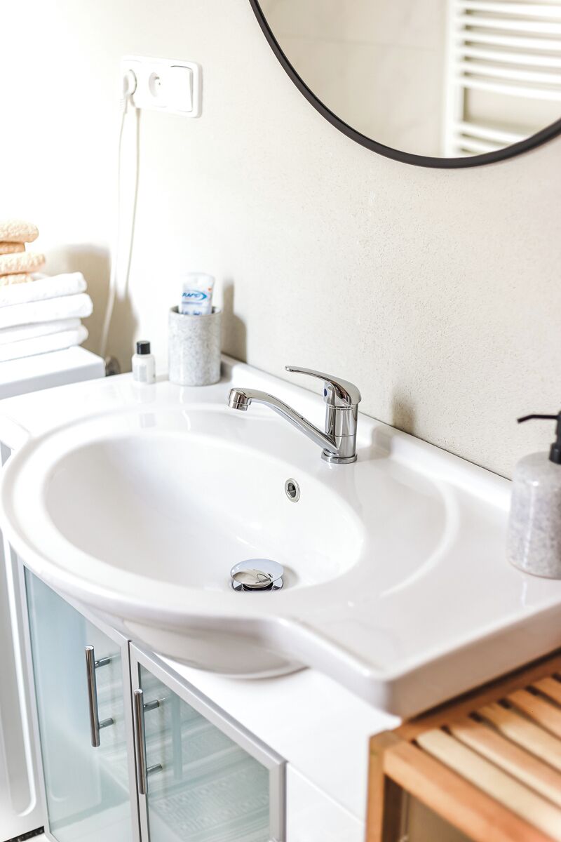 Un bagno con lavandino bianco, rubinetteria cromata e uno specchio. Sul lavandino ci sono articoli da toilette e uno porta asciugamani sopra.