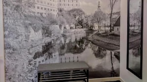 A room with a mural of a castle and river, a bench, and a framed picture on the wall.