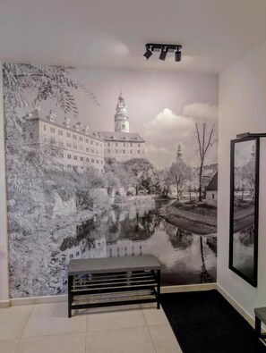 A room with a mural of a castle and river, a bench, and a framed picture on the wall.