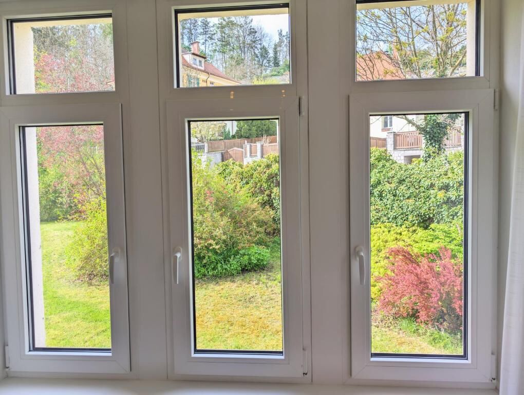 A set of three windows with a view of a garden and a house.