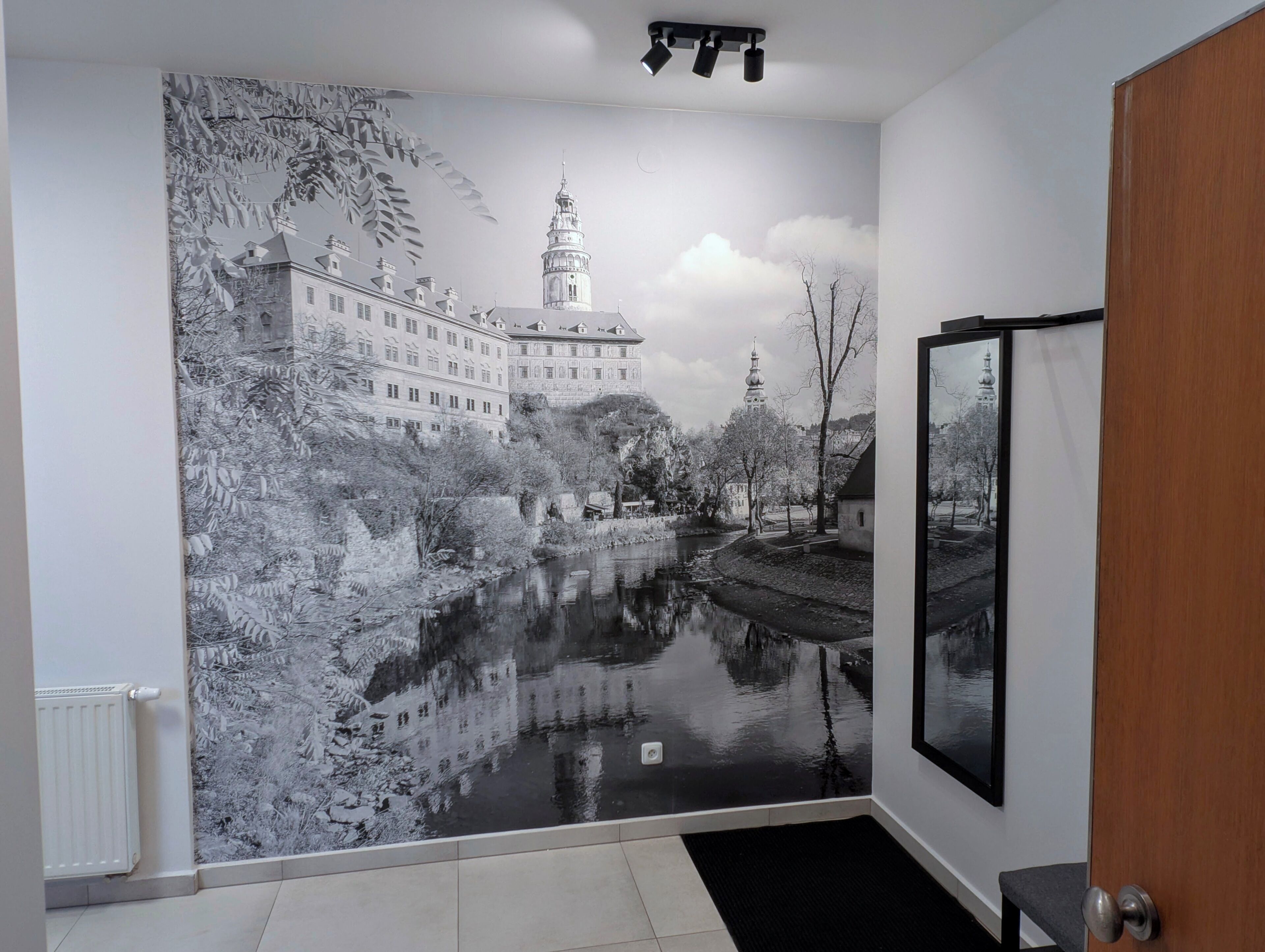 Une pièce ornée d’une grande fresque représentant un bâtiment historique et une rivière, avec une porte et un radiateur.