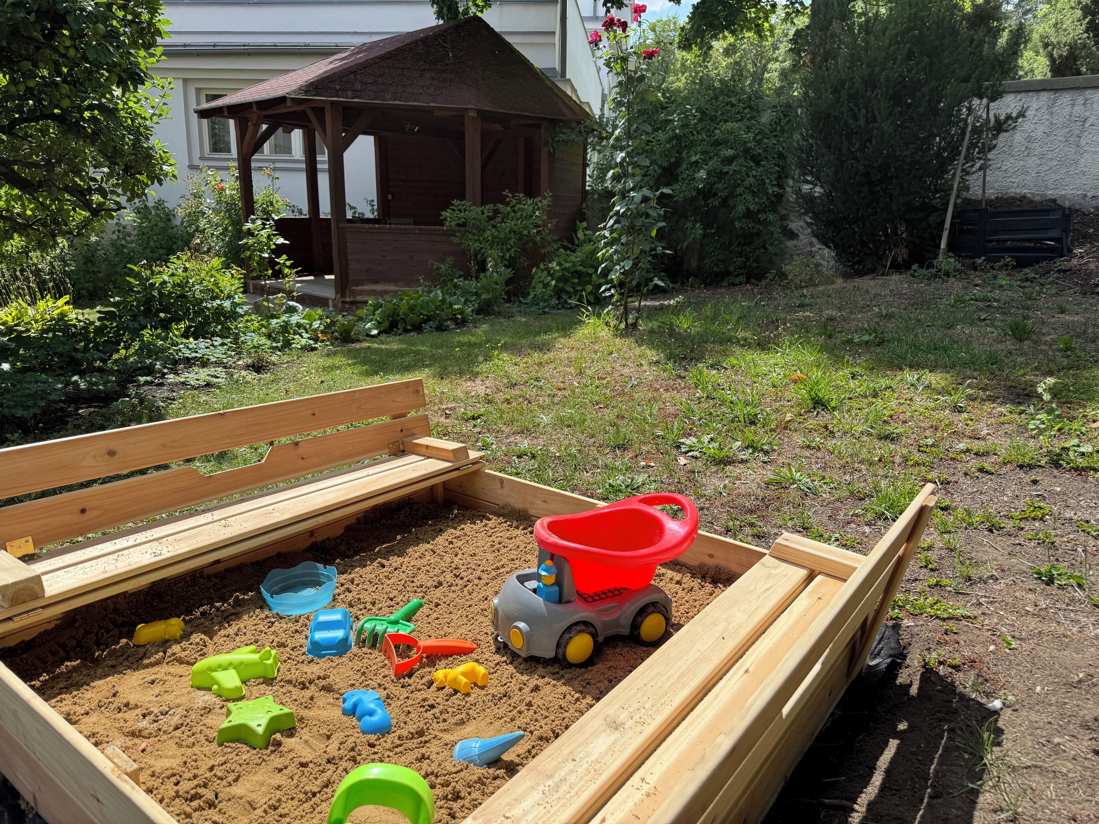 A sandbox with various toys and a small shed in a garden.