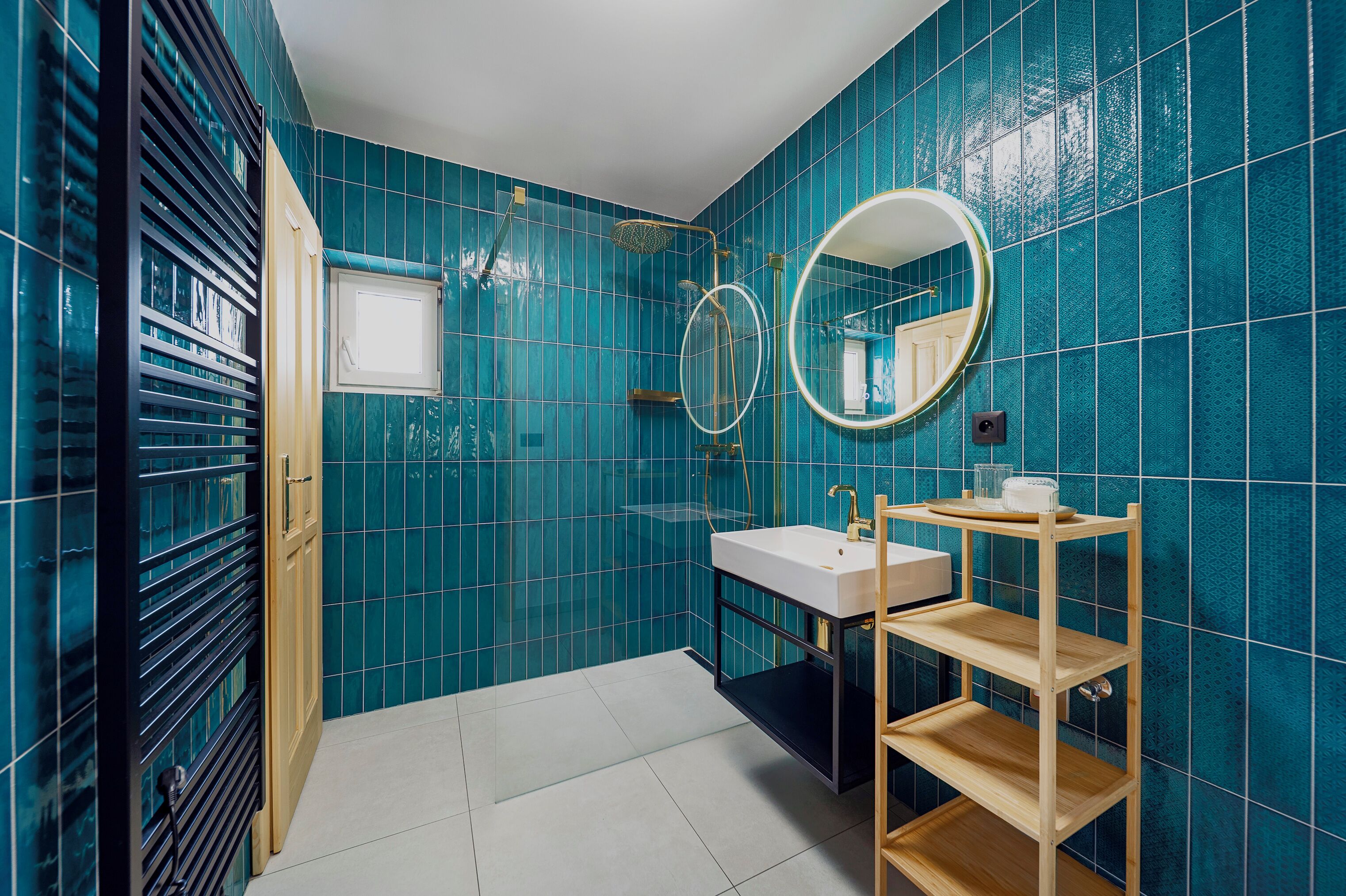 A bathroom with blue tiles, a white sink, a mirror, and a wooden shelf.