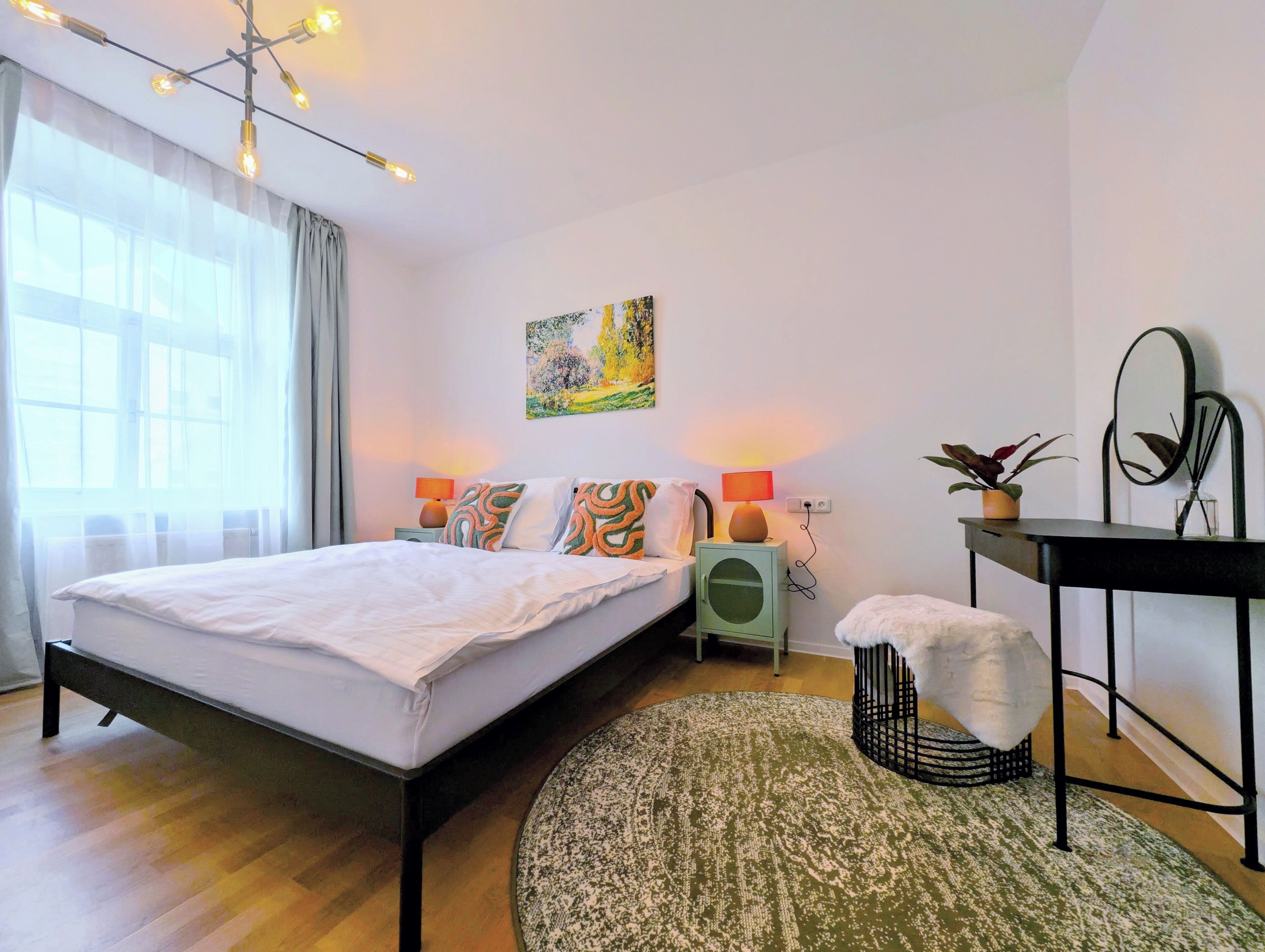 Une chambre à coucher moderne avec un grand lit, des lampes de chevet, une petite table, un miroir et un tableau accroché au mur.