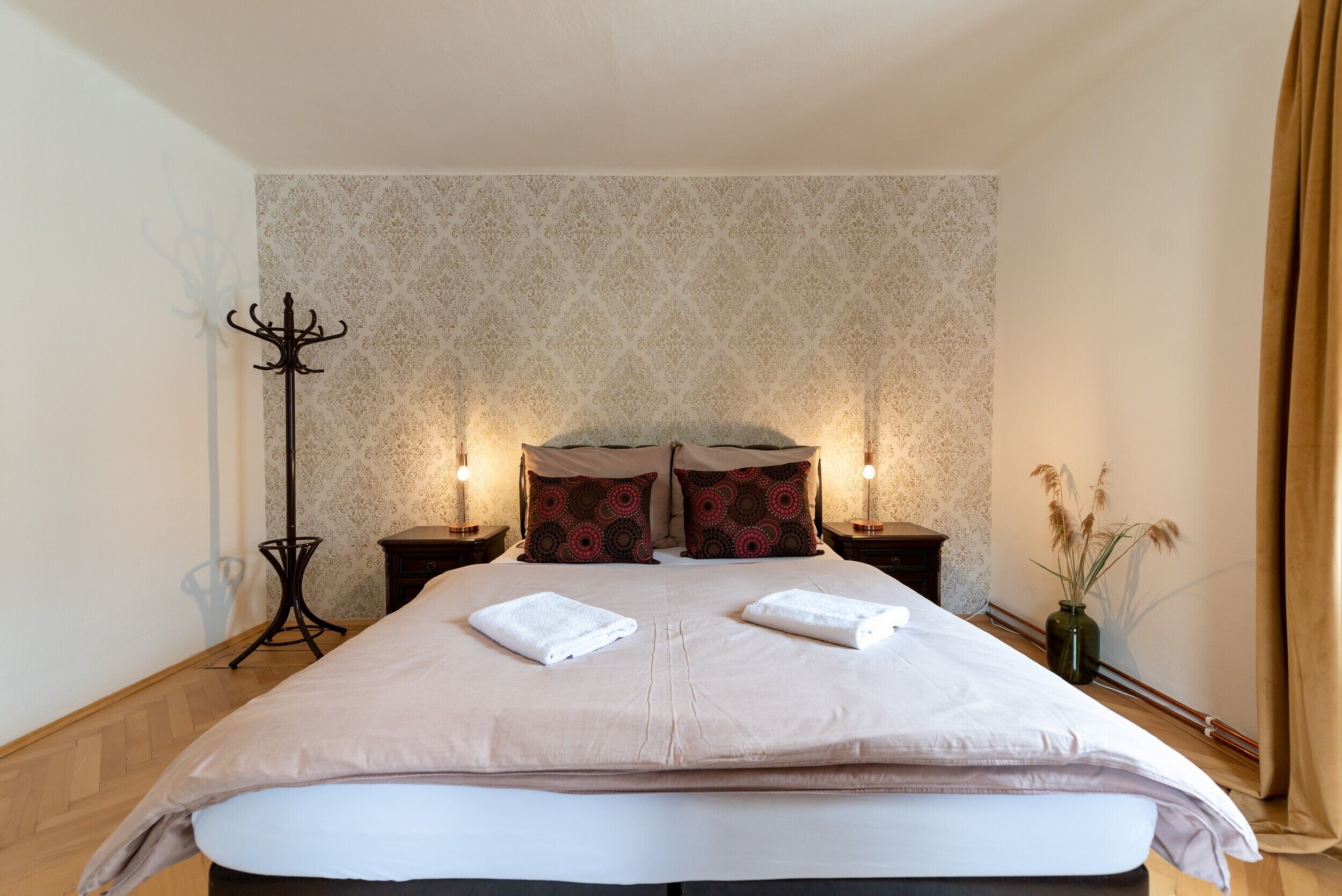 A neatly made bed with two pillows, a bedside table with a lamp, and a floor lamp.